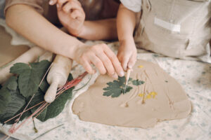 Duo parent Mère et fille façonnant ensemble de l’argile avec des feuilles lors d’un atelier Pitchoun’Art à Hourtin