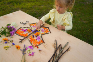 Petite fille réalisant un papillon avec des fleurs cueillies et des branches pendant un atelier créatif en pleine nature à Hourtin